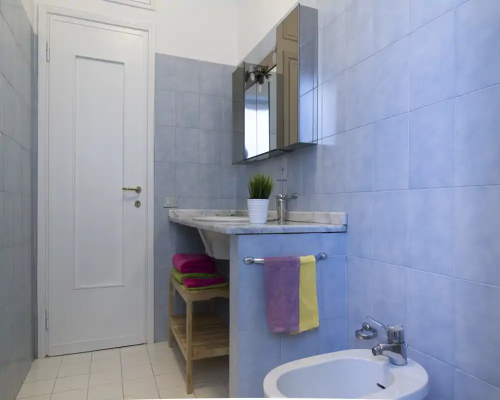 Baño limpio con azulejos azul claro, lavabo con encimera de mármol, armario con espejo, bidé y toallas de colores ordenadas.