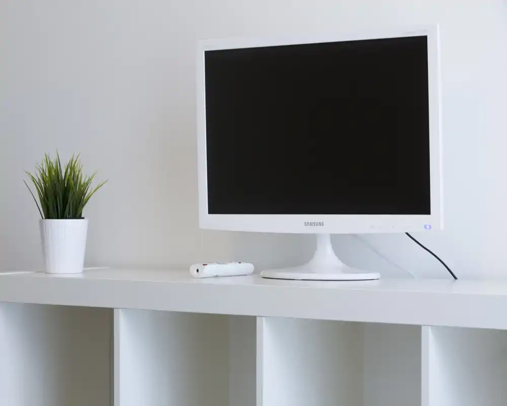 Minimal living-area detail with a white monitor on a clean white shelf and a small potted plant; bright, modern and very tidy styling.