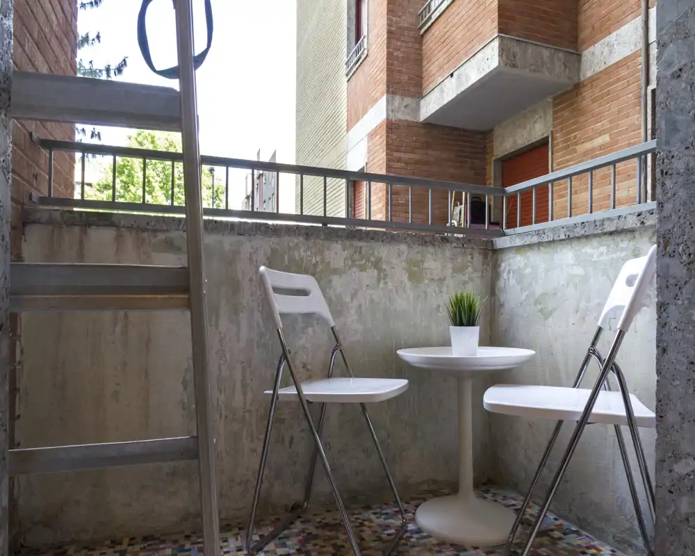Piccolo balcone privato con tavolino rotondo, due sedie pieghevoli e una pianta decorativa — ideale per il caffè mattutino in città.