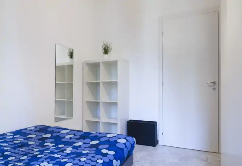 Bright minimal bedroom with a blue patterned bedspread, wall mirror and white cube shelving — clean, modern and easy to stage for listings.