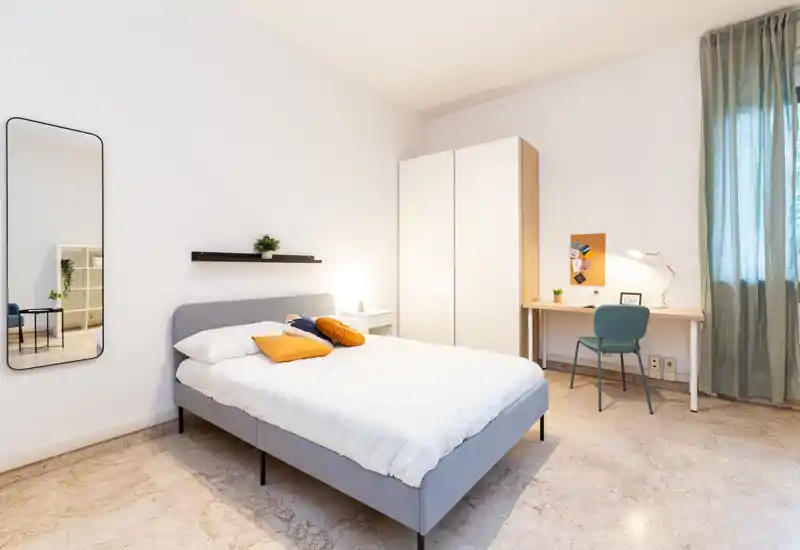 Bright, modern bedroom with a full double bed, bedside table, desk and wardrobe; minimal, cozy decor and clean lines ideal for rental listings.