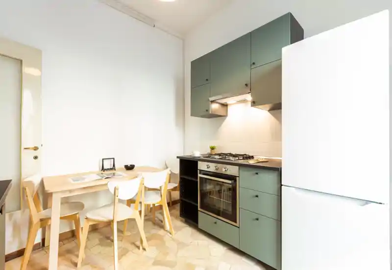 Cuisine moderne compacte avec meubles verts, four encastré et petite table avec quatre chaises ; espace lumineux, propre et fonctionnel, idéal pour un appartement en ville.
