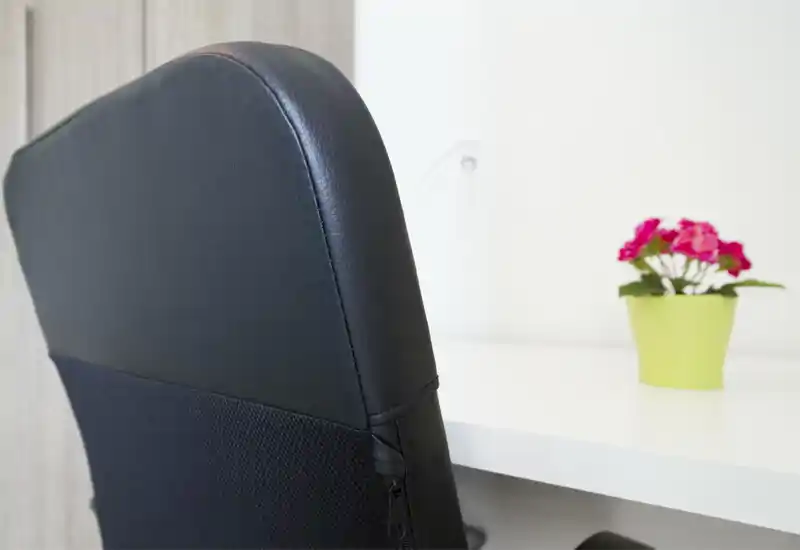 Primo piano di una sedia da scrivania moderna accanto a una scrivania bianca con un piccolo vaso di fiori; angolo di lavoro luminoso e minimal adatto a un soggiorno o home office.