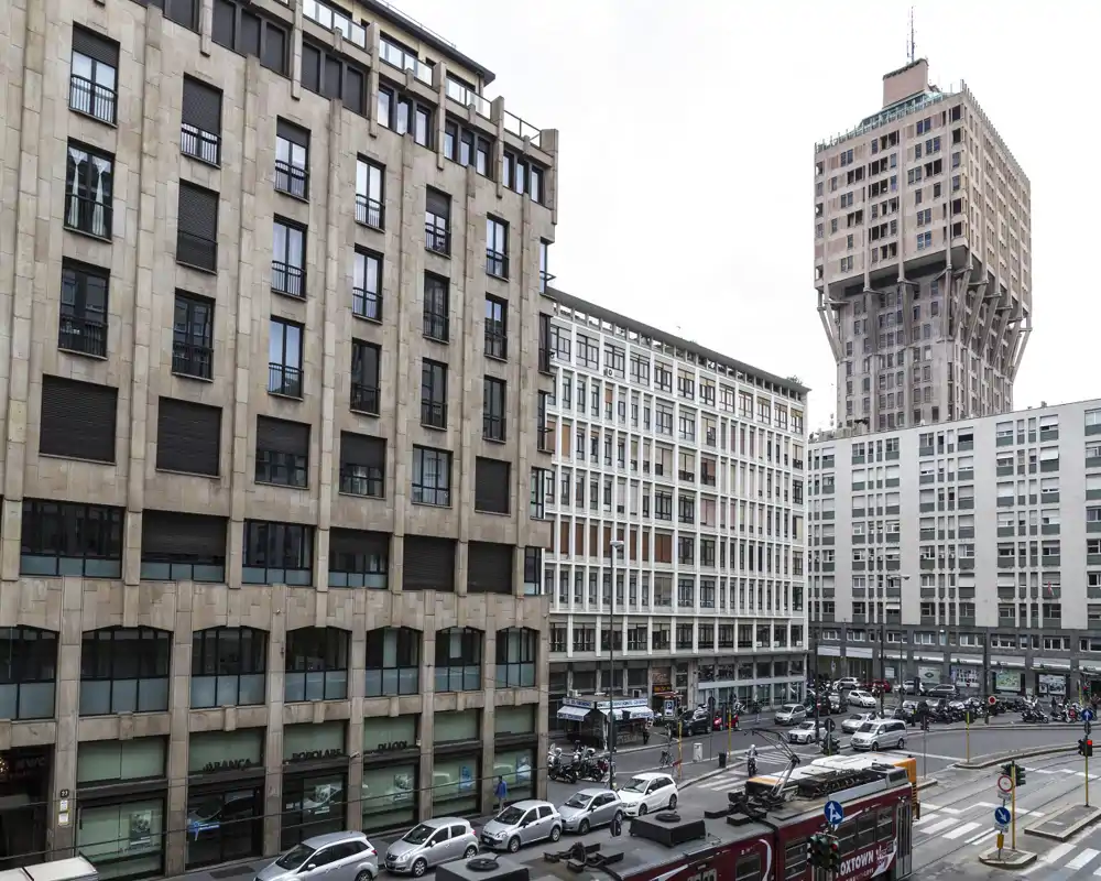 Veduta urbana con più facciate di edifici, auto parcheggiate e un incrocio trafficato con autobus e veicoli: utile per annunci che evidenziano la posizione cittadina o le finestre su strada.
