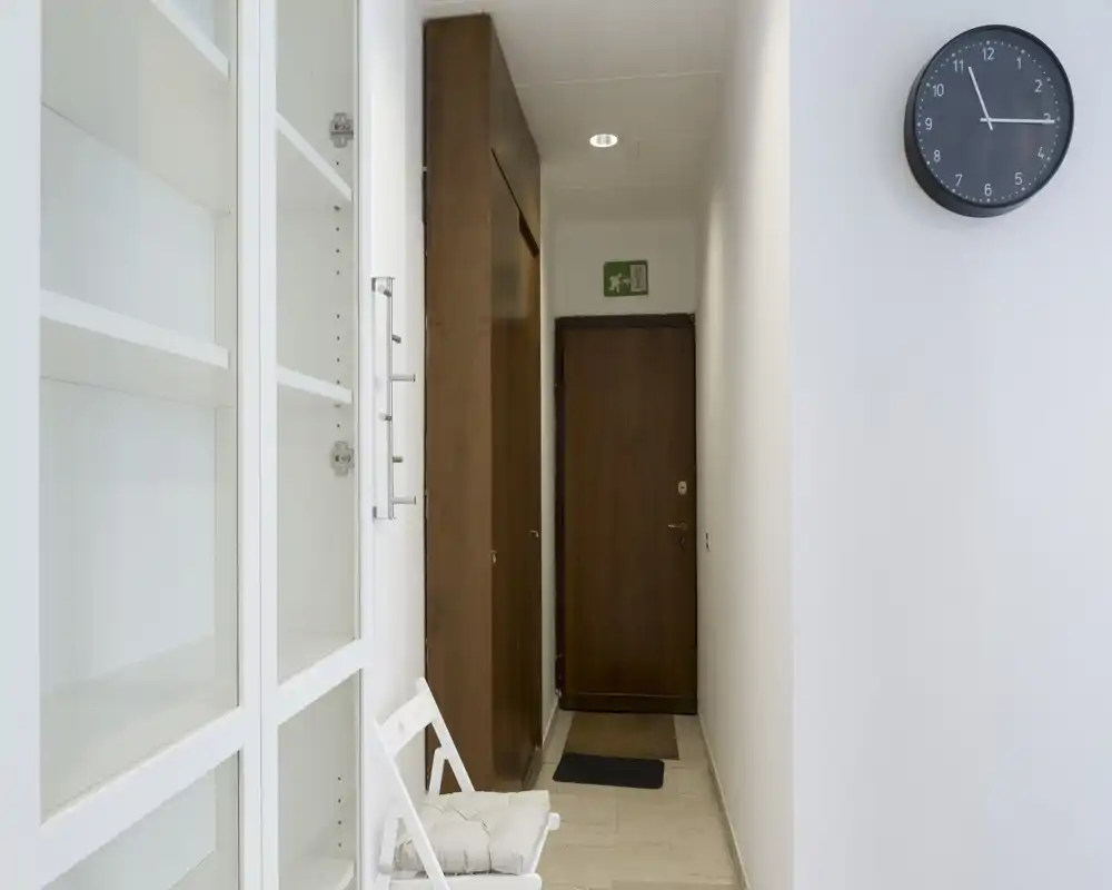 Ingresso stretto e ben illuminato con porta d’ingresso in legno, armadio a muro e una sedia semplice — stile minimale e pulito, ideale per la presentazione dell’appartamento.