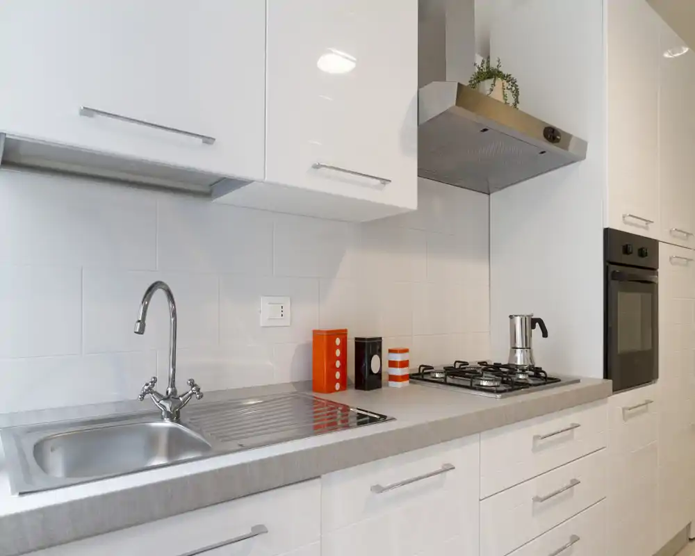Cucina moderna e luminosa con lavello in acciaio, piano cottura a gas e forno incassato; mobili bianchi lucidi e decorazioni minimal.