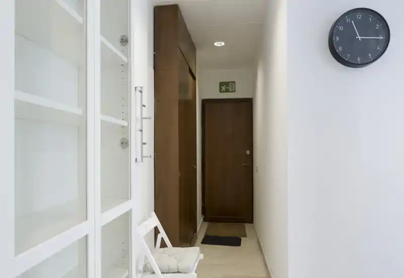 Ingresso stretto e ben illuminato con porta d’ingresso in legno, armadio a muro e una sedia semplice — stile minimale e pulito, ideale per la presentazione dell’appartamento.