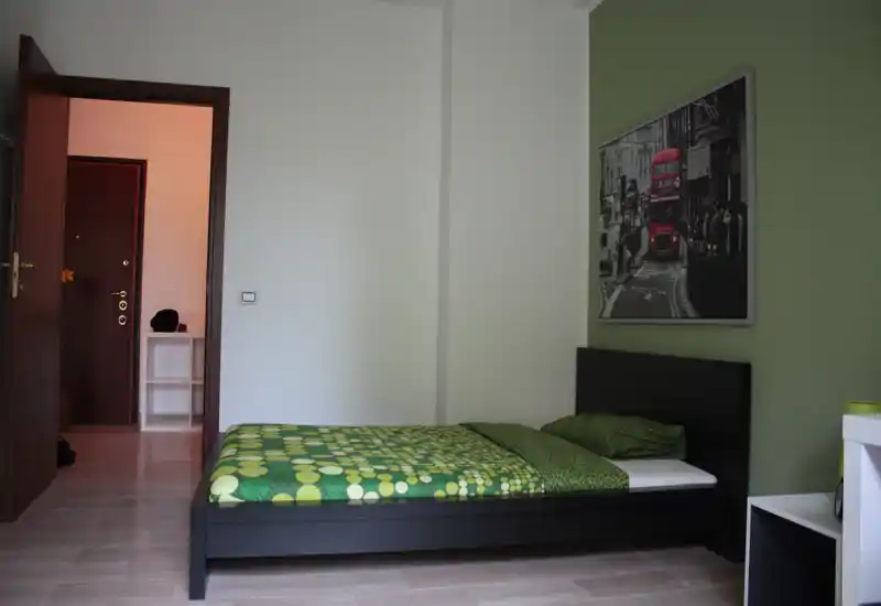 Dormitorio individual bien iluminado con cama de madera oscura moderna, ropa de cama verde a juego y cuadro decorativo. Estilo limpio y minimalista con buena luz natural, ideal para anuncios de alquiler.