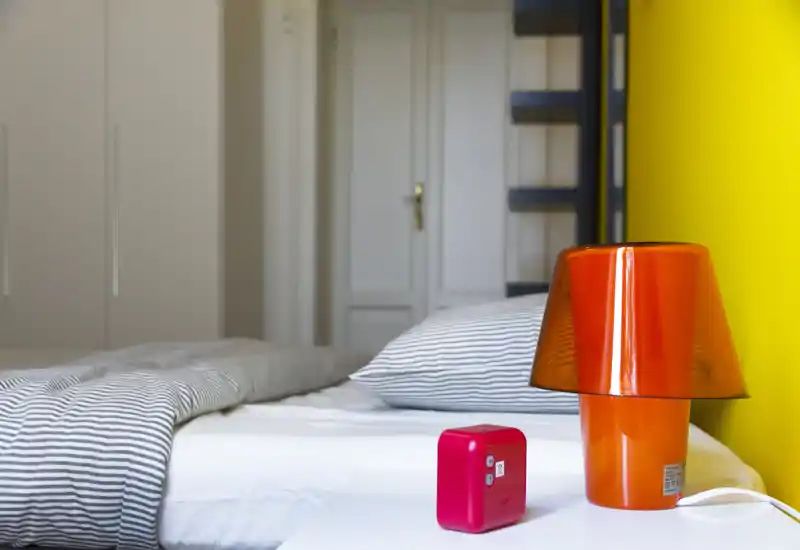 Camera da letto moderna e luminosa con piumone a righe e cuscino coordinato, una lampada arancione sul comodino e una parete gialla vivace che dona carattere.