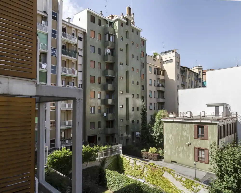 View of a residential inner courtyard and surrounding apartment façades with greenery and balconies, photographed from a balcony or window.