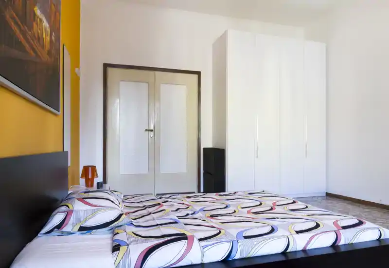 Bright, modern bedroom with a patterned double bed, clean white wardrobe and warm accent wall — ideal for rental photos highlighting space and style.