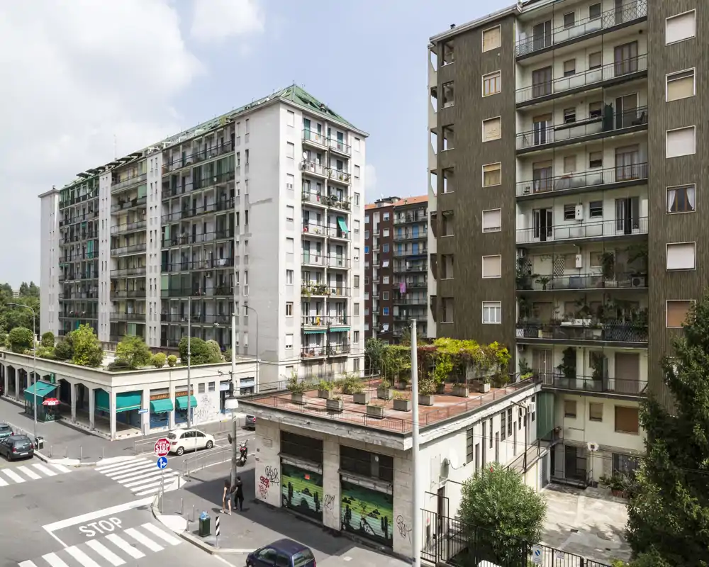 Scena urbana a livello strada con diversi palazzi residenziali, balconi e una terrazza sul tetto; ideale per mostrare la posizione e gli esterni.