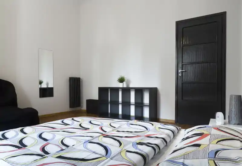 Camera da letto luminosa e moderna con biancheria da letto a motivo, mensola semplice e pareti bianche pulite che creano uno spazio minimal e confortevole.