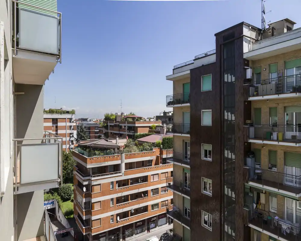 Balcone luminoso con vista sui palazzi residenziali e cielo sereno — perfetto per mostrare lo spazio esterno e il contesto urbano.