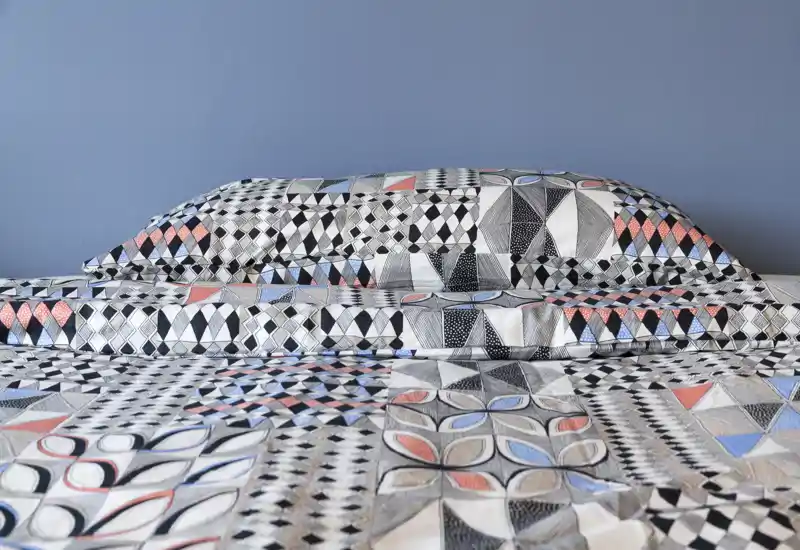 Bright, well-composed bedroom close-up showing a neatly made bed with patterned duvet and pillows against a soft blue wall — ideal for listing photos highlighting bedding and room style.