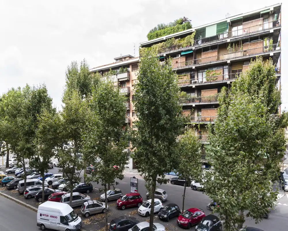 Exterior urban view showing a residential building facade, tree-lined street and parked cars — suitable for listing the building or neighborhood location.
