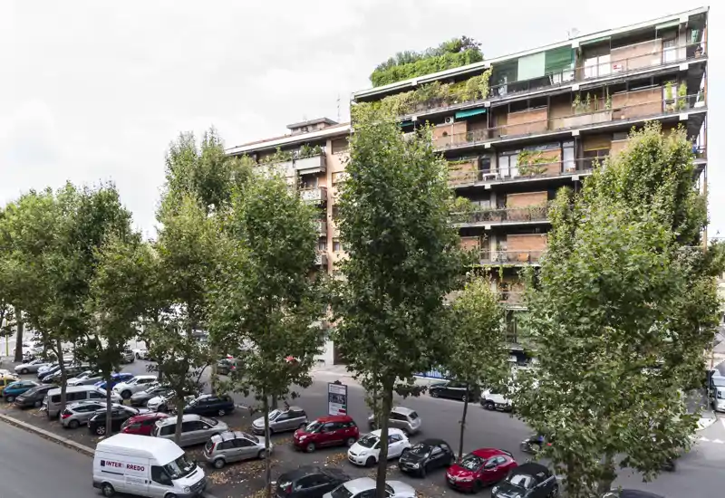 Veduta esterna urbana con la facciata di un edificio residenziale, strada alberata e auto parcheggiate — adatta per descrivere l’edificio o la posizione nel quartiere.
