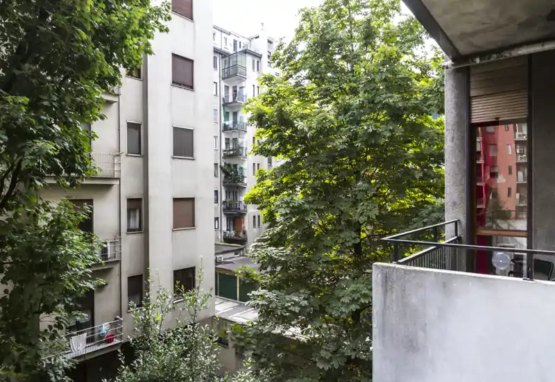 Vista dal balcone in città con alberi maturi e facciate di condomini vicini; il verde offre privacy e una vista tranquilla.