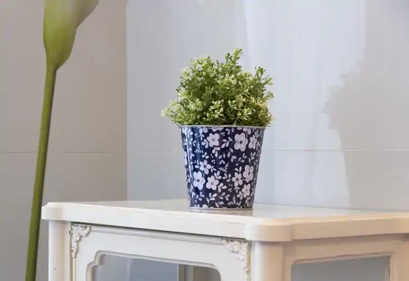 Angolo decorativo con una pianta in vaso floreale su un tavolino bianco ornamentale; immagine luminosa e pulita adatta come dettaglio d'arredo per il soggiorno.