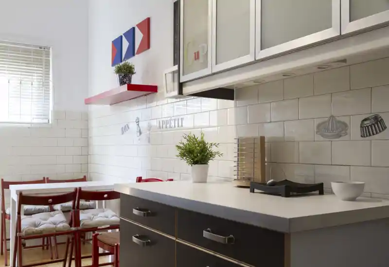 Cucina compatta e luminosa con paraschizzi in piastrelle bianche, piano di lavoro con cassettoni e un piccolo angolo pranzo con sedie rosse — accogliente e ben arredata per un annuncio.