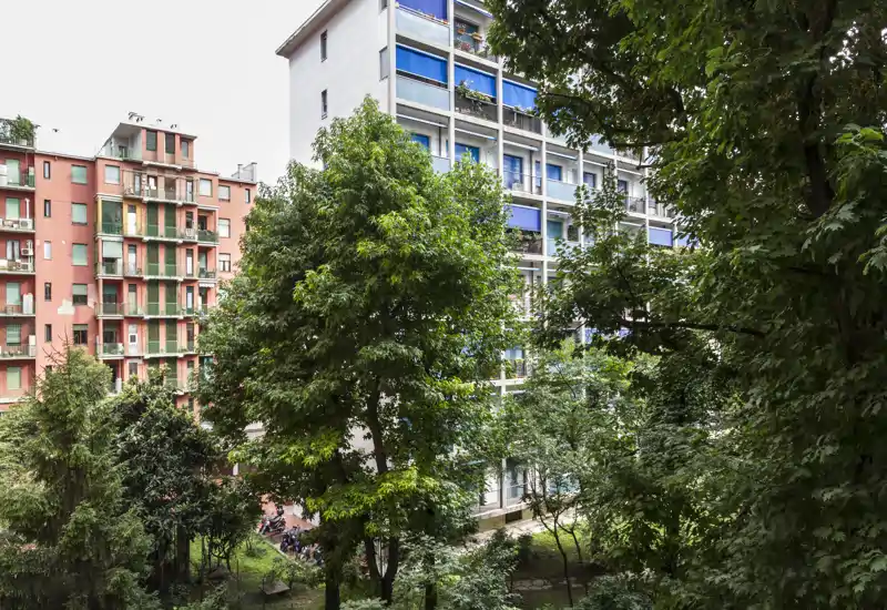 Veduta di un cortile alberato e dei palazzi adiacenti, con alberi verdi e balconi — ideale per mostrare un'area esterna condominiale tranquilla.