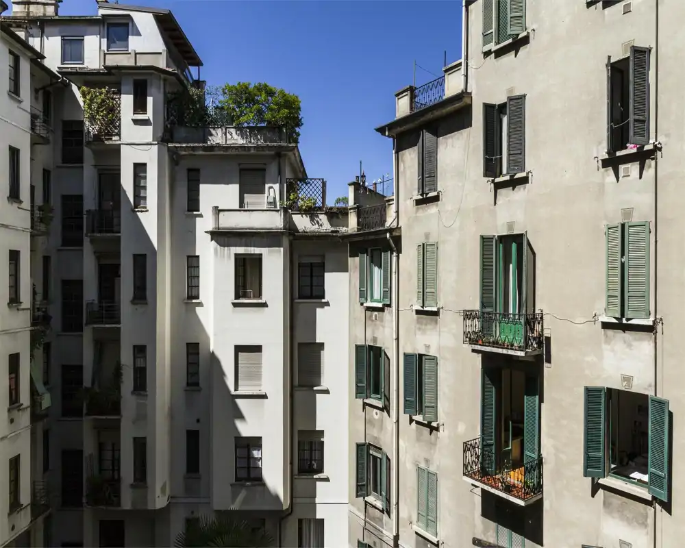 Vue extérieure des immeubles autour d'une cour intérieure, montrant façades, volets verts et balcons sous un ciel bleu clair.