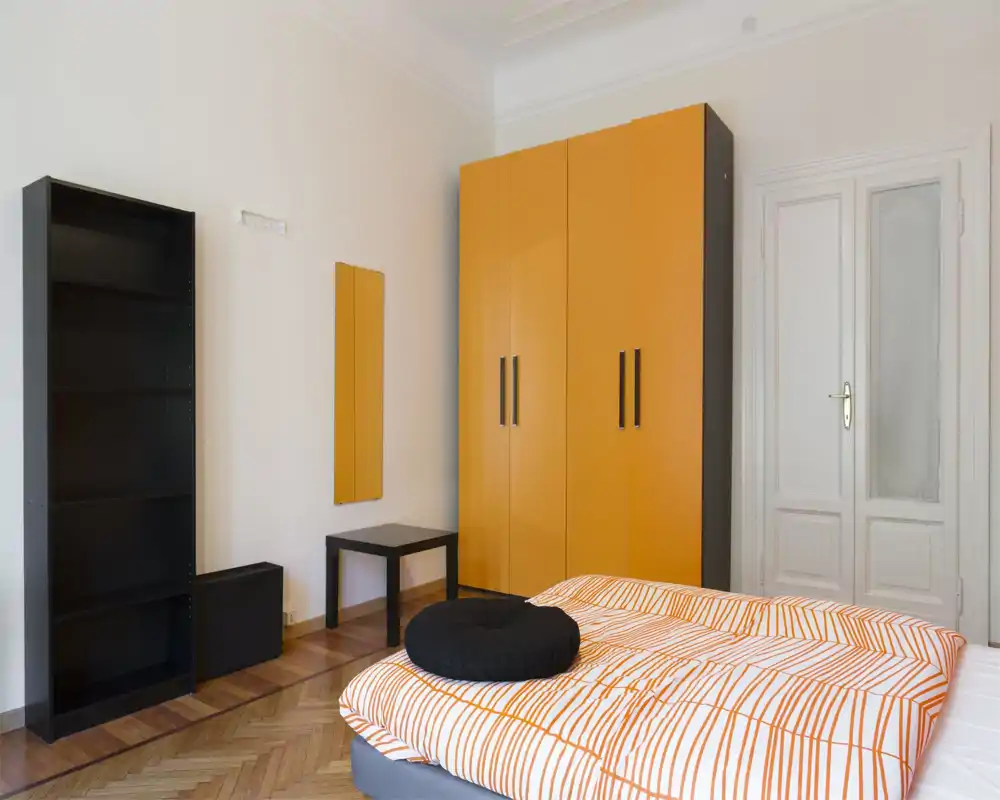 Dormitorio moderno y luminoso con edredón de rayas naranja y blanco, cama baja y armario naranja a juego. Mobiliario minimalista, suelo de parquet y líneas limpias crean un espacio cómodo para dormir.