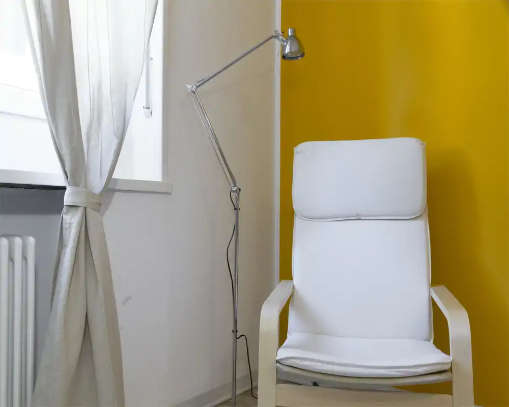 Angolo luminoso e moderno con una comoda poltrona bianca, una lampada da terra regolabile e una parete gialla calda—ideale per leggere o rilassarsi vicino alla finestra.