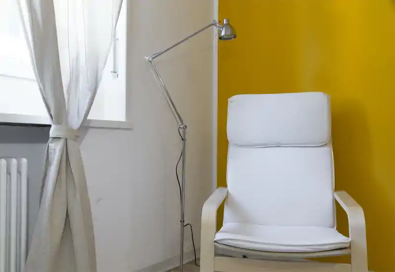 Bright, modern corner with a comfortable white armchair, adjustable floor lamp and a warm yellow accent wall—ideal for reading or relaxing by the window.