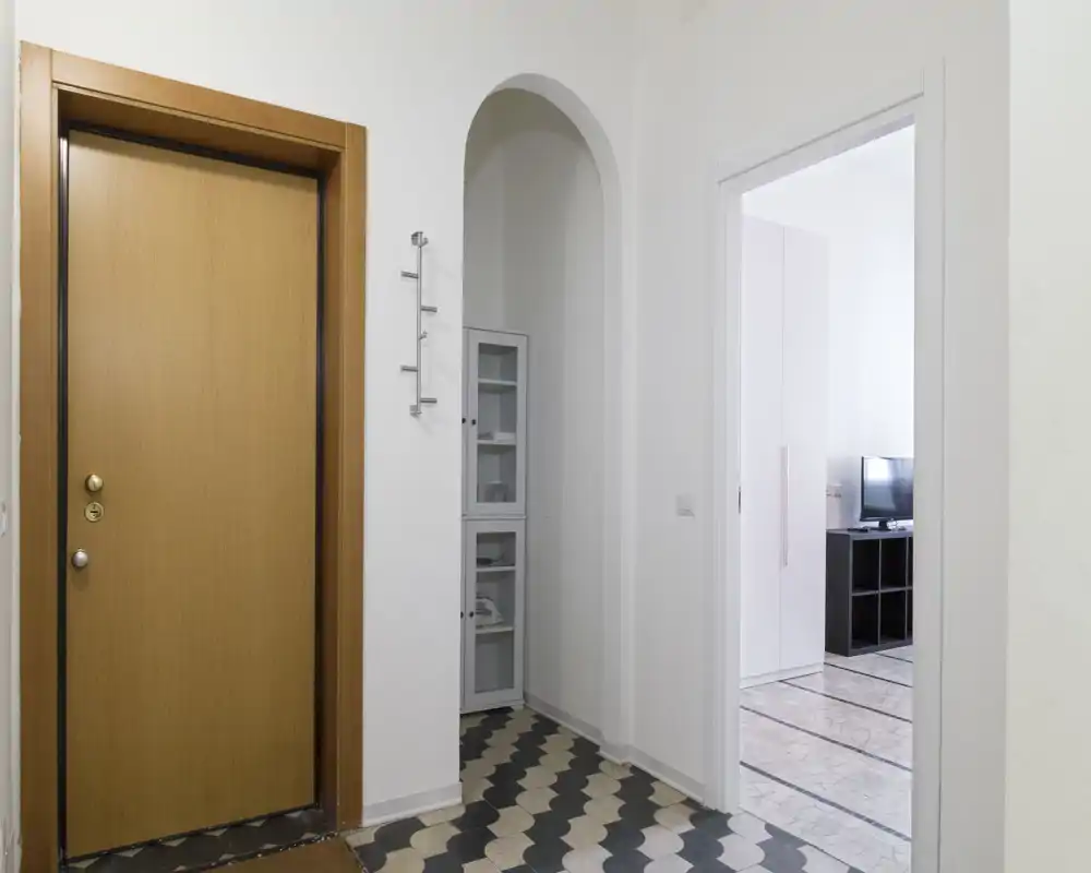 Ingresso luminoso e pulito con porta d'ingresso in legno, pavimento a piastrelle ornamentali e un nicchia ad arco con vano di servizio.