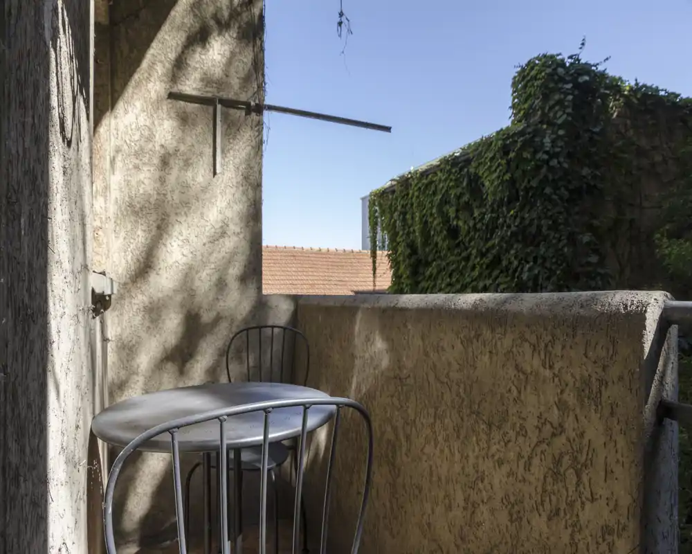 Piccolo balcone privato con tavolino tondo in metallo e due sedie, soleggiato con vista su vegetazione — ideale per il caffè mattutino.