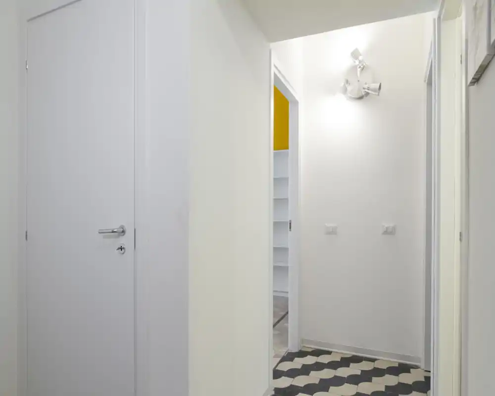 Ingresso minimal e luminoso con pavimento a motivo, pareti bianche e applique moderna — accesso funzionale alle stanze adiacenti.