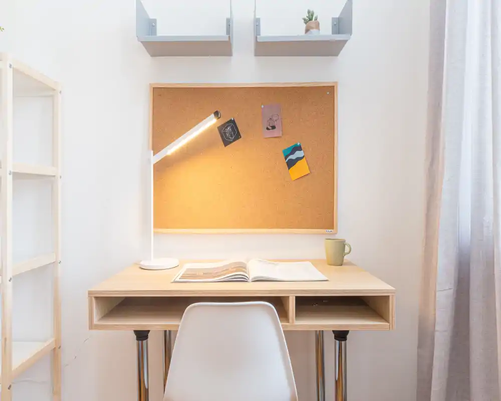 Angolo studio ordinato con scrivania in legno, lampada da tavolo, bacheca in sughero e sedia comoda — spazio di lavoro luminoso e minimal, perfetto per smartworking o lettura.