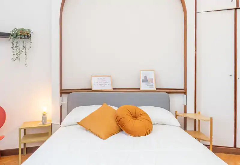 Bright, well-staged bedroom with a large bed centered in the frame, warm mustard cushions and soft white bedding creating a cozy, modern look.