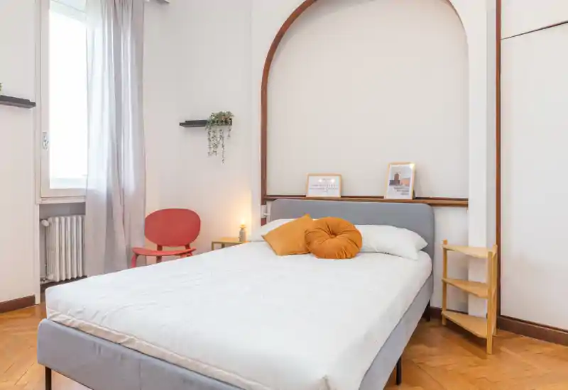 Sunny, stylish bedroom with a full double bed, soft textiles and warm decorative accents; bright natural light from the window and tasteful minimal decor.