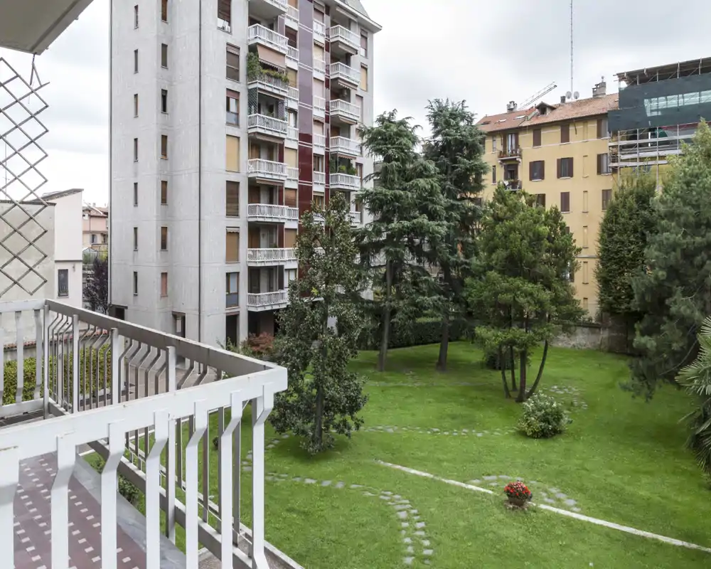 Vista desde el balcón hacia un patio ajardinado comunitario con árboles y edificios alrededor, ideal para destacar el espacio exterior.