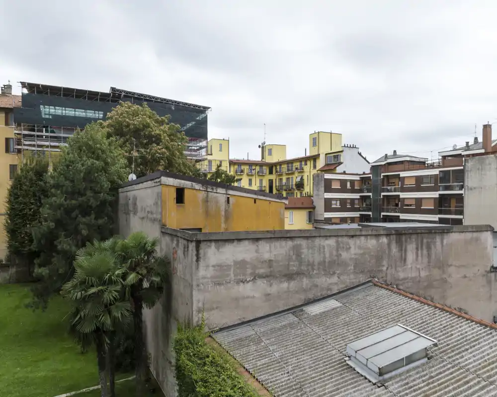 Patio urbano y tejados vecinos visto desde una ventana, con árboles y fachadas de apartamentos bajo un cielo nublado.