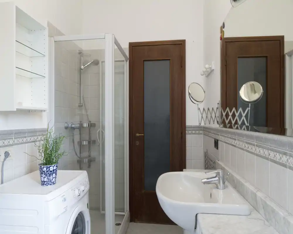 Baño luminoso y bien cuidado con ducha, lavabo con espejo y lavadora; azulejos neutros y accesorios prácticos que lo hacen funcional y limpio.