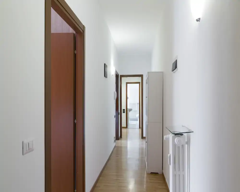 Pasillo de entrada largo y luminoso con suelo de madera, paredes blancas y puertas hacia las habitaciones; decoración mínima e iluminación práctica que crean un paso limpio y acogedor.