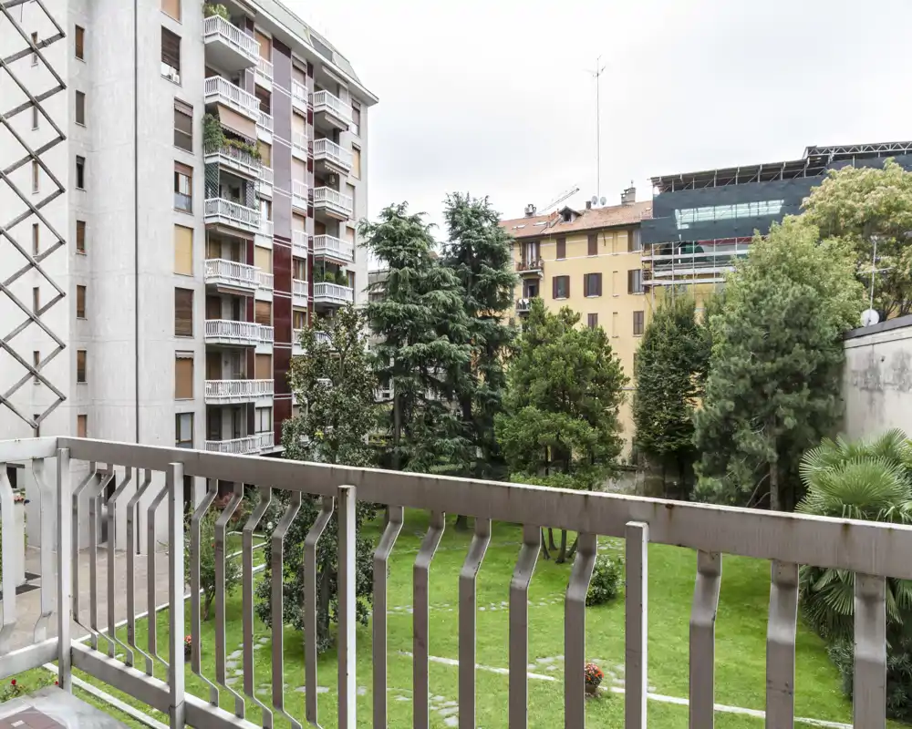 Vista desde el balcón hacia un patio ajardinado con árboles y edificios vecinos — agradable espacio exterior urbano.
