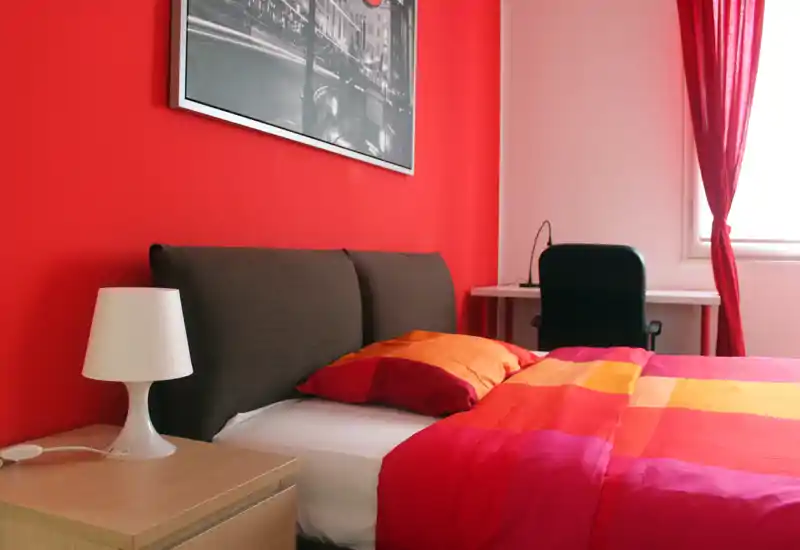 Bright, colorful bedroom with a double bed, warm textiles and a small desk by the window — ideal for a modern city stay.