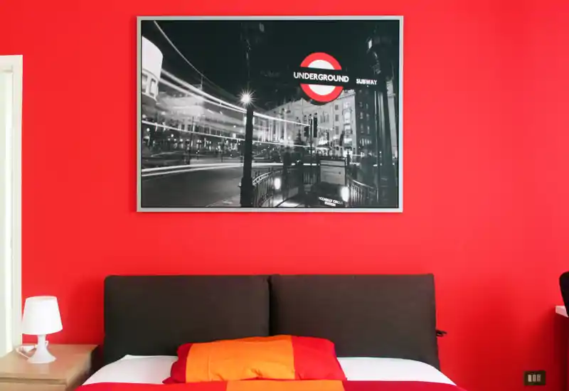 Bright styled bedroom with a dark upholstered headboard, colorful orange and red bedding and a striking black-and-white framed print above the bed.