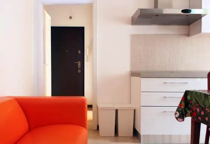 Bright, modern living area with a bold orange sofa next to a compact kitchenette; clean lines and warm accents create a welcoming space.