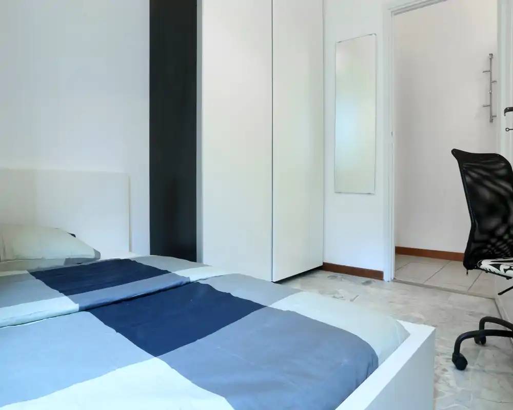 Dormitorio moderno y luminoso con cama doble arreglada, armario blanco y suelo efecto mármol — espacio minimalista ideal para estancias cortas.