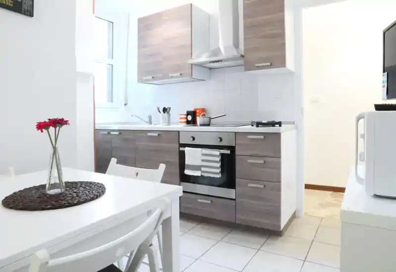Cocina moderna y luminosa con muebles efecto madera, horno empotrado, placa de gas y una pequeña mesa — espacio limpio y bien iluminado, ideal para alquileres de corta estancia.