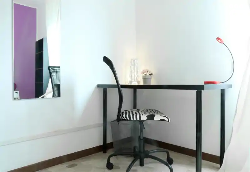 Bright, minimal home office corner with a black desk, patterned swivel chair, small lamp and potted plant — ideal for focused work in a compact space.