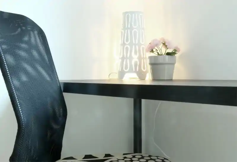 Bright, minimal desk corner with a modern mesh chair, a decorative table lamp and a small potted plant — ideal for a compact home office or study nook.