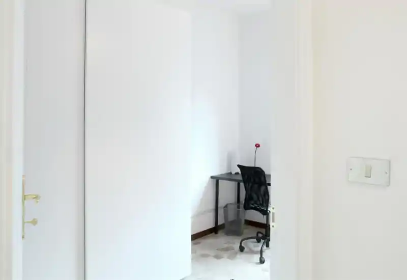 Small bright workspace visible through an open doorway with a simple desk, task chair and lamp — ideal for a compact home office or study corner.
