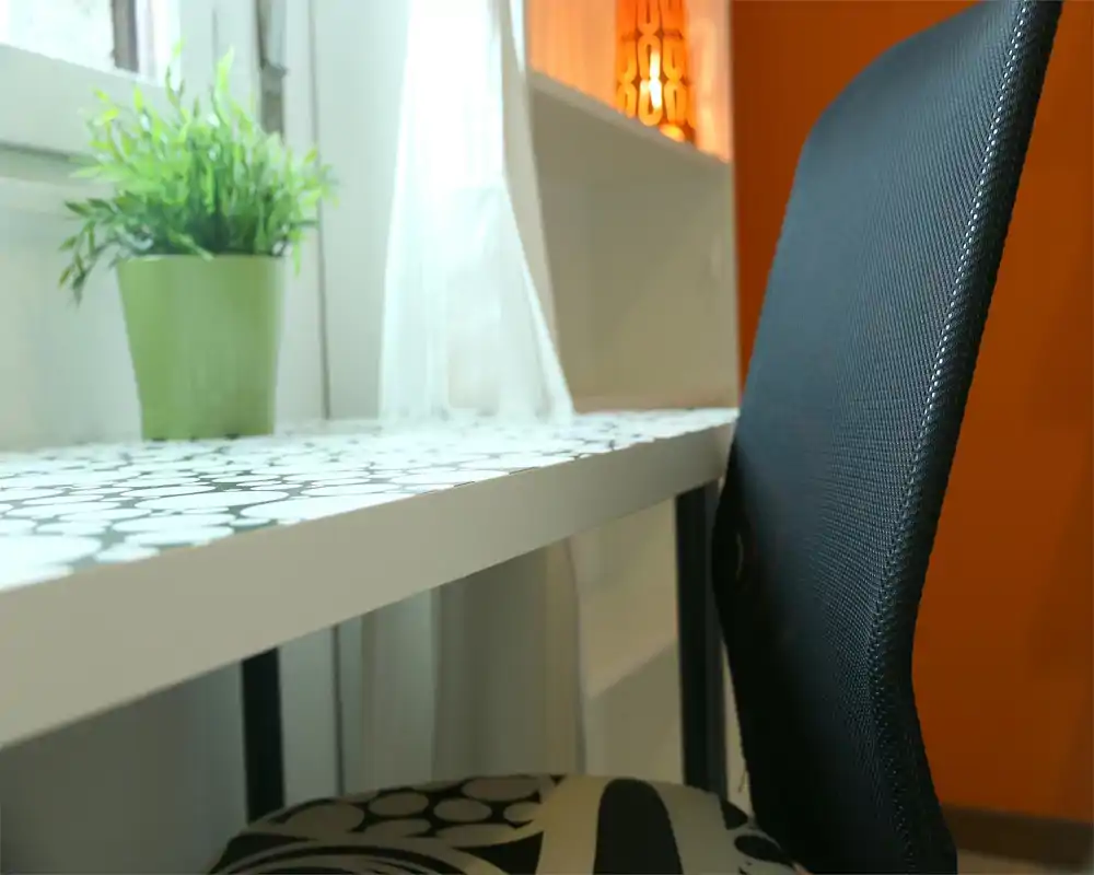 Angolo luminoso con scrivania decorata, vaso con pianta e moderna sedia nera da ufficio — un angolo living/lavoro accogliente e ben illuminato vicino alla finestra.