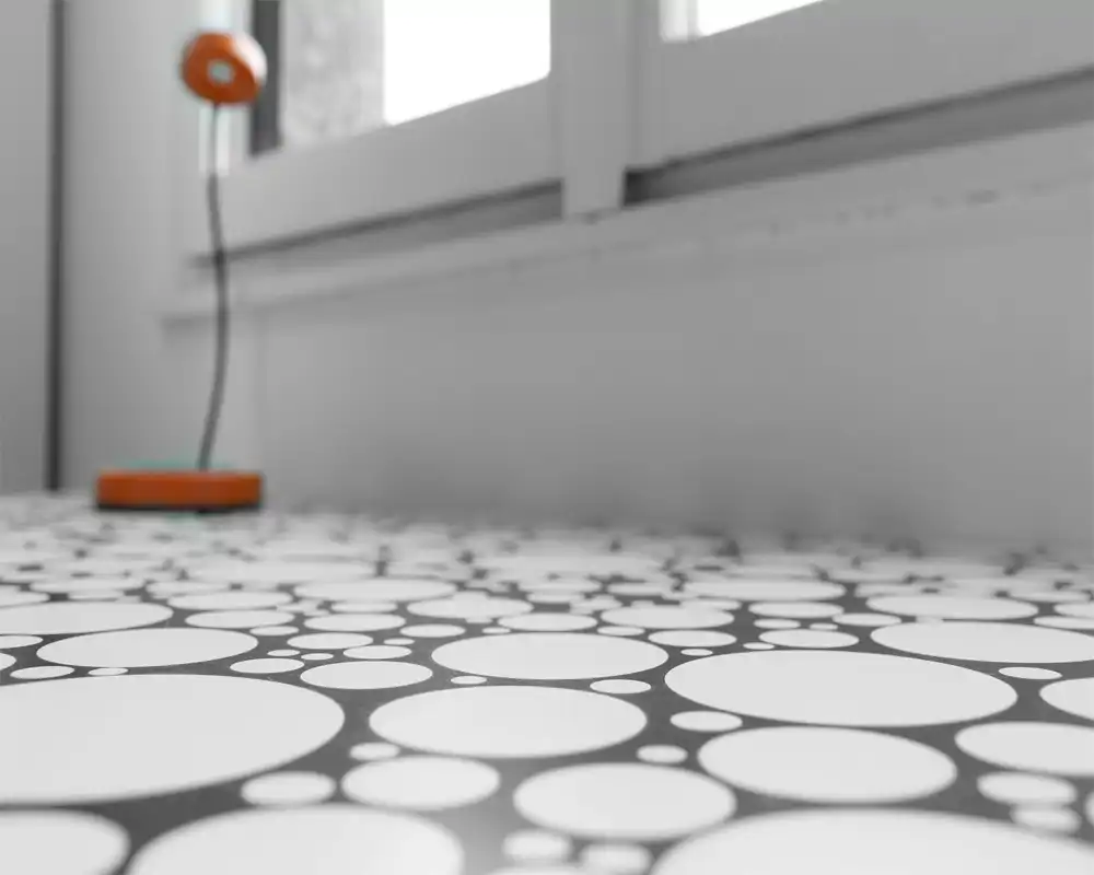 Primo piano di una superficie con motivo a cerchi e una lampada sfocata davanti a una finestra. L'immagine mette in risalto il motivo e la texture, non la funzione di una stanza.